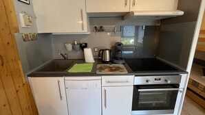 Una cocina compacta con armarios blancos, lavavajillas integrado, cafetera y horno pequeño.
