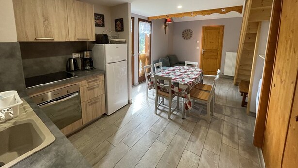 A compact kitchen with wooden cabinets, a refrigerator, and a dining area with a table and chairs. - Charming 50m² Chalet Apartment - WiFi, Ski Storage, Near Slopes & Shuttle (Le Lioran)