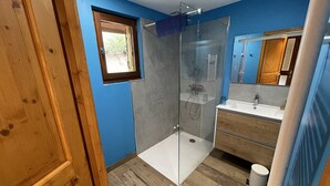 A modern bathroom with a glass shower enclosure, a wooden vanity, and a small window. - Charming 50m² Chalet Apartment - WiFi, Ski Storage, Near Slopes & Shuttle (Le Lioran)