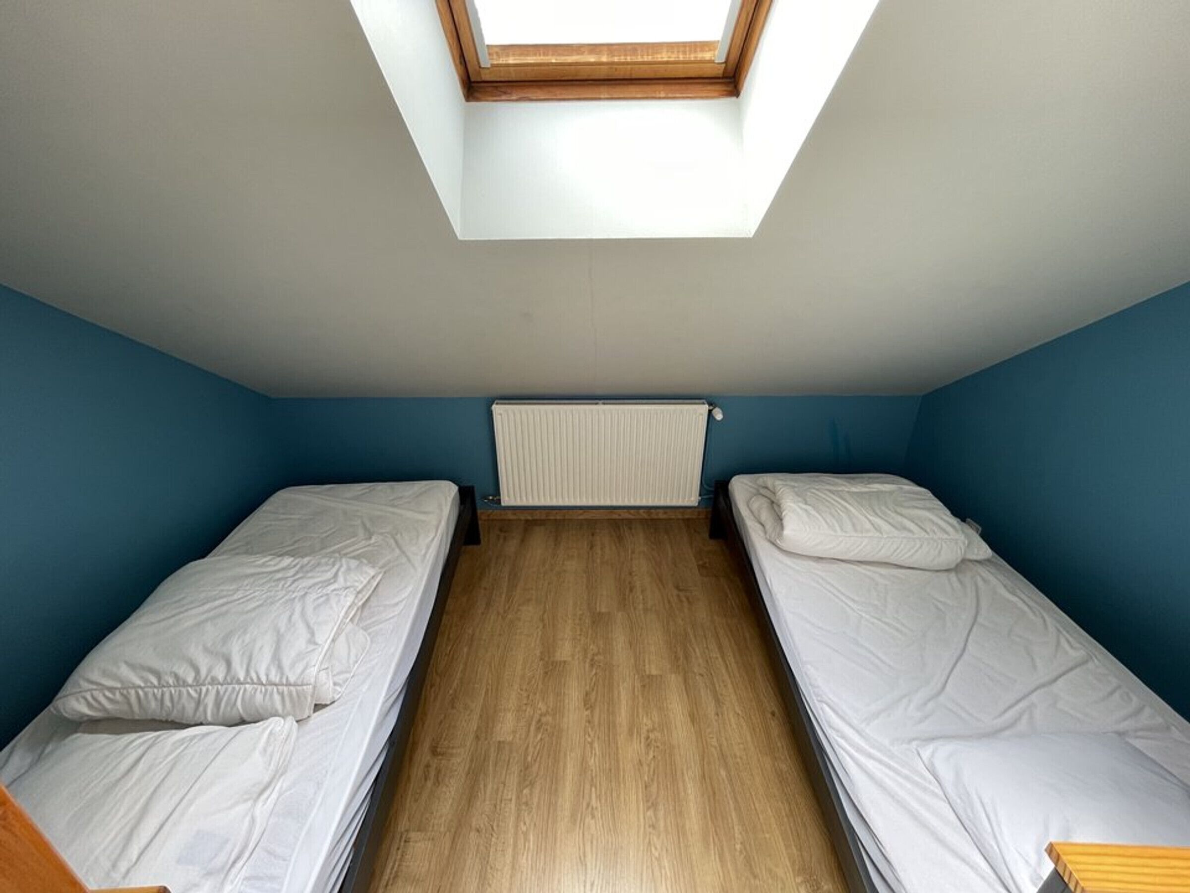 Un petit dortoir d’une seule pièce, comprenant deux lits simples, une lucarne et un radiateur.