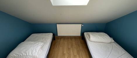 Un petit dortoir d’une seule pièce, comprenant deux lits simples, une lucarne et un radiateur.