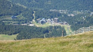 A mountainous landscape with a small cluster of buildings, including a large hotel with multiple structures, surrounded by dense forest. - Charming 50m² Chalet Apartment - WiFi, Ski Storage, Near Slopes & Shuttle (Le Lioran)