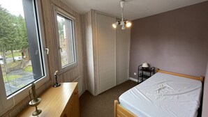 A bedroom with a wooden bed, a desk with a lamp, a window, and a ceiling fan. - Cozy T2 in Station Center, Near Shops and Slopes (Le Lioran)