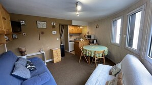 A compact living space with a blue sofa, a white bed, a small kitchen area, and a dining table. - Cozy T2 in Station Center, Near Shops and Slopes (Le Lioran)