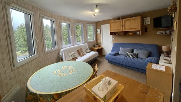 A cozy living room with a round table, a blue sofa, and a wooden cabinet. - Cozy T2 in Station Center, Near Shops and Slopes (Le Lioran)
