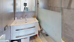A modern bathroom with a large mirror, a white vanity with a sink, and a glass shower enclosure. - Quiet Apartment with Terrace, Parking, and AC, 5 Min Drive to Beach (Frontignan)