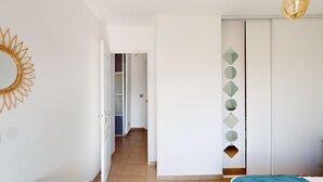 A bedroom with a bed, a wardrobe, a mirror, and a hallway leading to a bathroom. - Quiet Apartment with Terrace, Parking, and AC, 5 Min Drive to Beach (Frontignan)