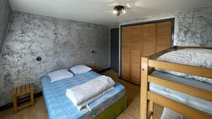A bedroom with a bunk bed, a single bed, a wooden stool, a wardrobe, and a ceiling light fixture.