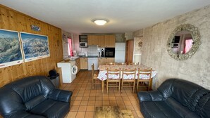 A compact living space with a kitchen, dining area, and two black leather sofas.