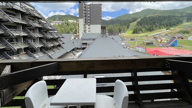 A view from a balcony with a table and chairs, overlooking a building with a sloped roof and a tall structure in the background. - Ski-in/Ski-out Studio, South-East Balcony, Sleeps 4, Shops Onsite (Le Lioran)
