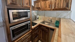 A compact kitchen with built-in appliances, wooden cabinets, and a marble backsplash. - Ski-in/Ski-out Studio, South-East Balcony, Sleeps 4, Shops Onsite (Le Lioran)