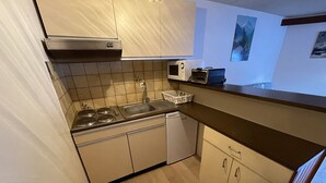A compact kitchen with a stove, sink, and dishwasher. There are cabinets and a microwave on the countertop.