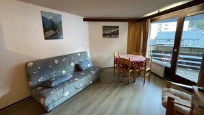 A living room with a sofa, a dining table with chairs, and a balcony with a view.