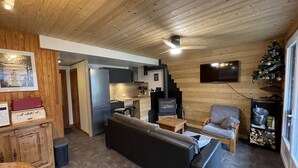 A cozy cabin interior with a wooden ceiling, a sofa, a TV, and a fireplace.