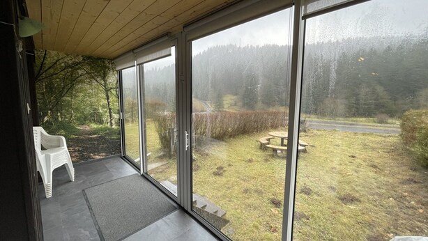 A covered porch with large glass doors leading to a grassy outdoor area with a picnic table and a chair.