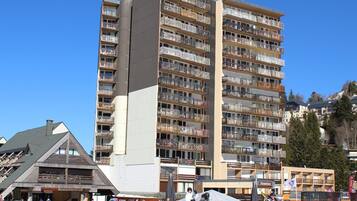 Een hotel met meerdere verdiepingen, balkons, ski-uitrusting en een piste op de voorgrond.