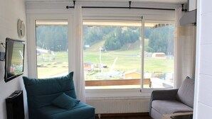 A modern living room with a large window, a sofa, a television, and a radiator. - Ski-in/Ski-out Studio with Balcony and WiFi in Laveissière (Le Lioran)