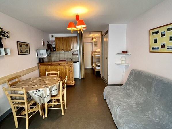 A compact living space with a dining area, kitchenette, and a sofa. - Cozy Studio with South-Facing Terrace, Close to Amenities, Ski Lifts, and Skating Rink (Le Lioran)