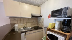 A compact kitchen with a sink, stove, microwave, and a coffee maker on a shelf. - Central Duplex with Balcony – Sleeps 6/8, Pets Welcome (Le Lioran)
