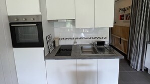 A compact kitchen with white cabinets, a built-in oven, a sink, and a small countertop. - Central studio with balcony and WiFi (Le Lioran)