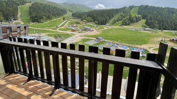 A balcony with a view of a rural landscape, including green fields, a road, and buildings. - Central studio with balcony and WiFi (Le Lioran)
