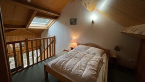 A bedroom with a wooden bed, a nightstand with a lamp, a skylight, and a view of a balcony.
