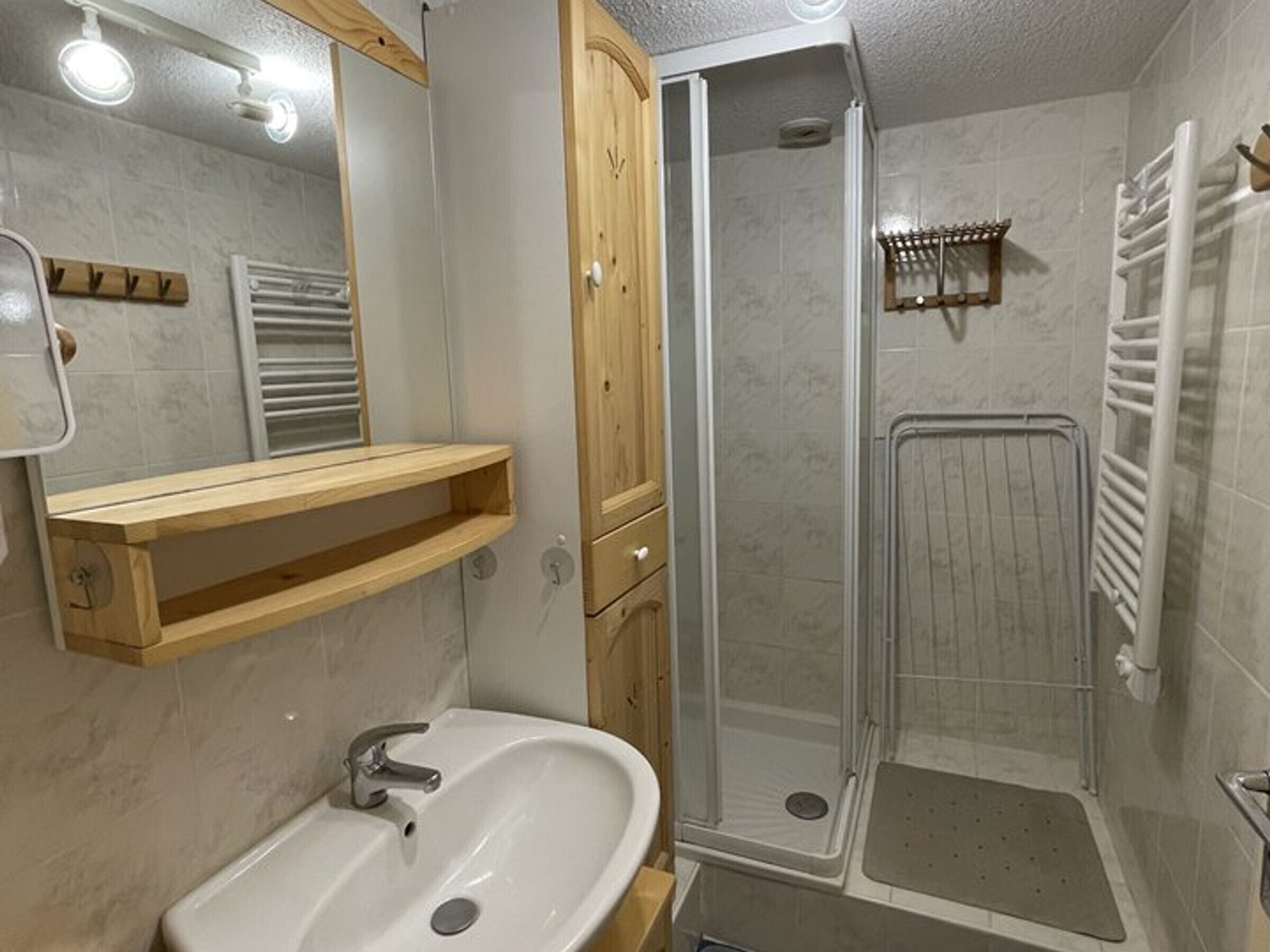 A bathroom with a sink, mirror, wooden cabinet, and a shower enclosure.