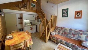 A cozy interior with a dining area, kitchen, and a loft bedroom with a wooden staircase. - Cozy South-Facing Studio with Mezzanine, Near Slopes, Ski Shuttle, & Free Parking (Le Lioran)