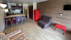 A modern living space with a kitchen, dining area, and a seating area with a sofa and a small table. - Studio with Balcony, Equipped Kitchen, Wi-Fi in Le Lioran (Le Lioran)