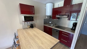 A compact kitchen with a wooden table, red cabinets, a microwave, a sink, and a coffee maker. - Studio with Balcony, Equipped Kitchen, Wi-Fi in Le Lioran (Le Lioran)