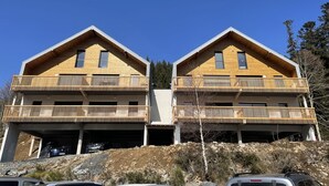 A modern two-story wooden house with balconies, a garage, and a clear blue sky. - Cozy New 2-BR Apartment with Large Balcony, Close to Chairlift (Le Lioran)