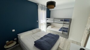 A compact hotel room with a single bed, a bunk bed, a small table, and a wardrobe. - Cozy New 2-BR Apartment with Large Balcony, Close to Chairlift (Le Lioran)