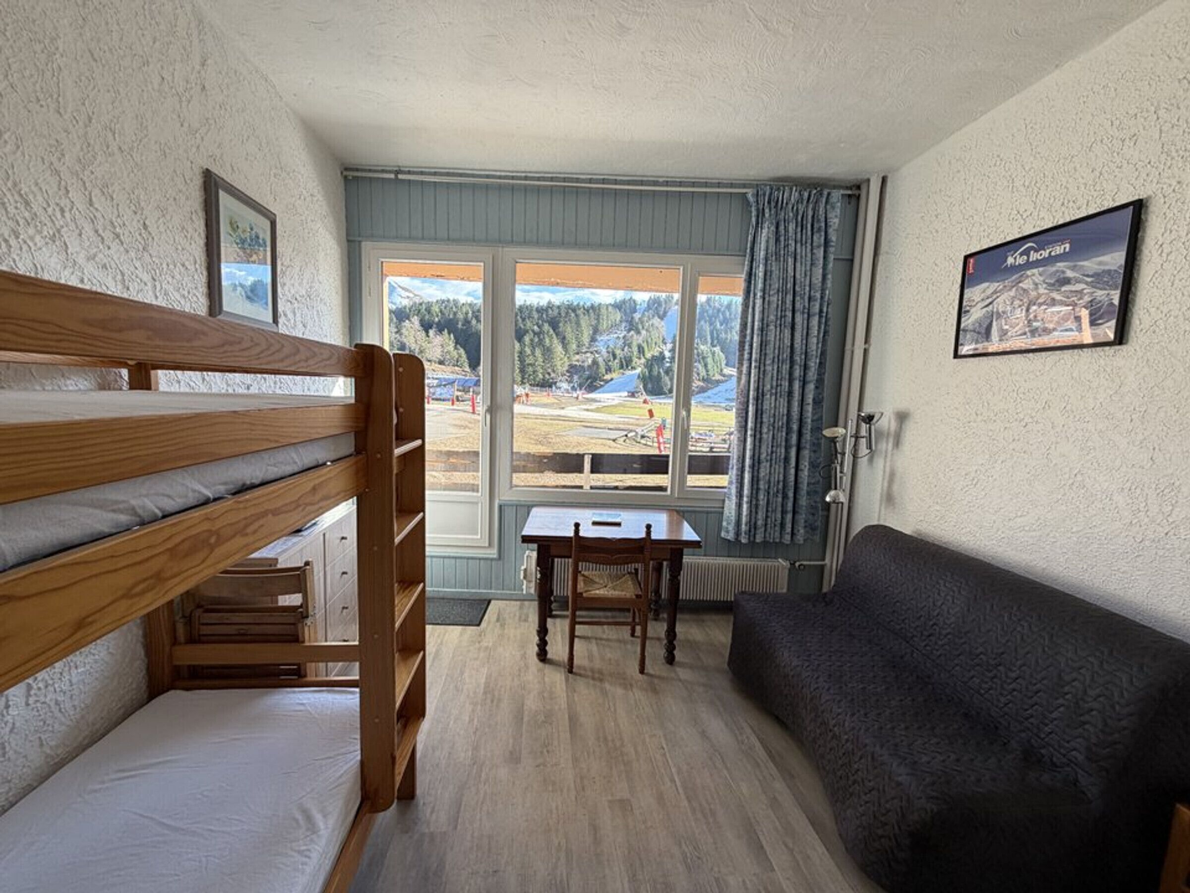 A room with bunk beds, a desk, a couch, and a window with a view of a forest and mountains.