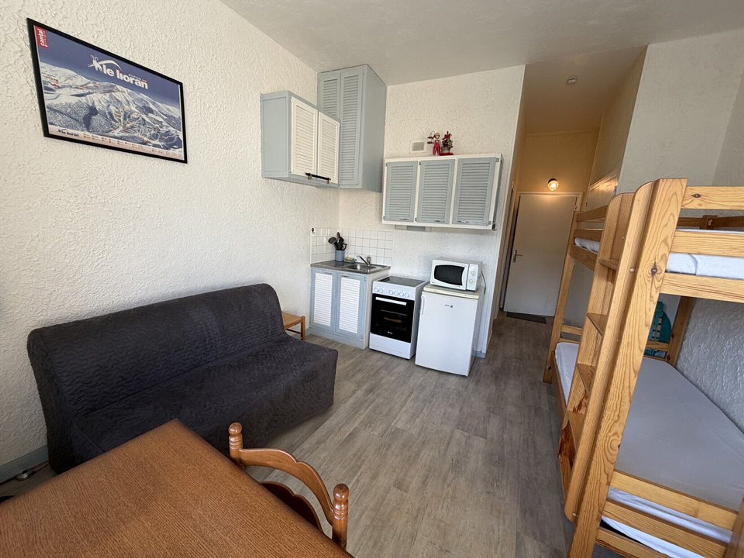 A compact room with a sofa, bunk beds, a kitchenette, and a framed picture on the wall.