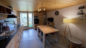 A compact kitchen with wooden cabinets, a dining table, and a view through the windows. - Charming duplex near slopes with balcony and parking (Saint-Jacques-des-Blats)