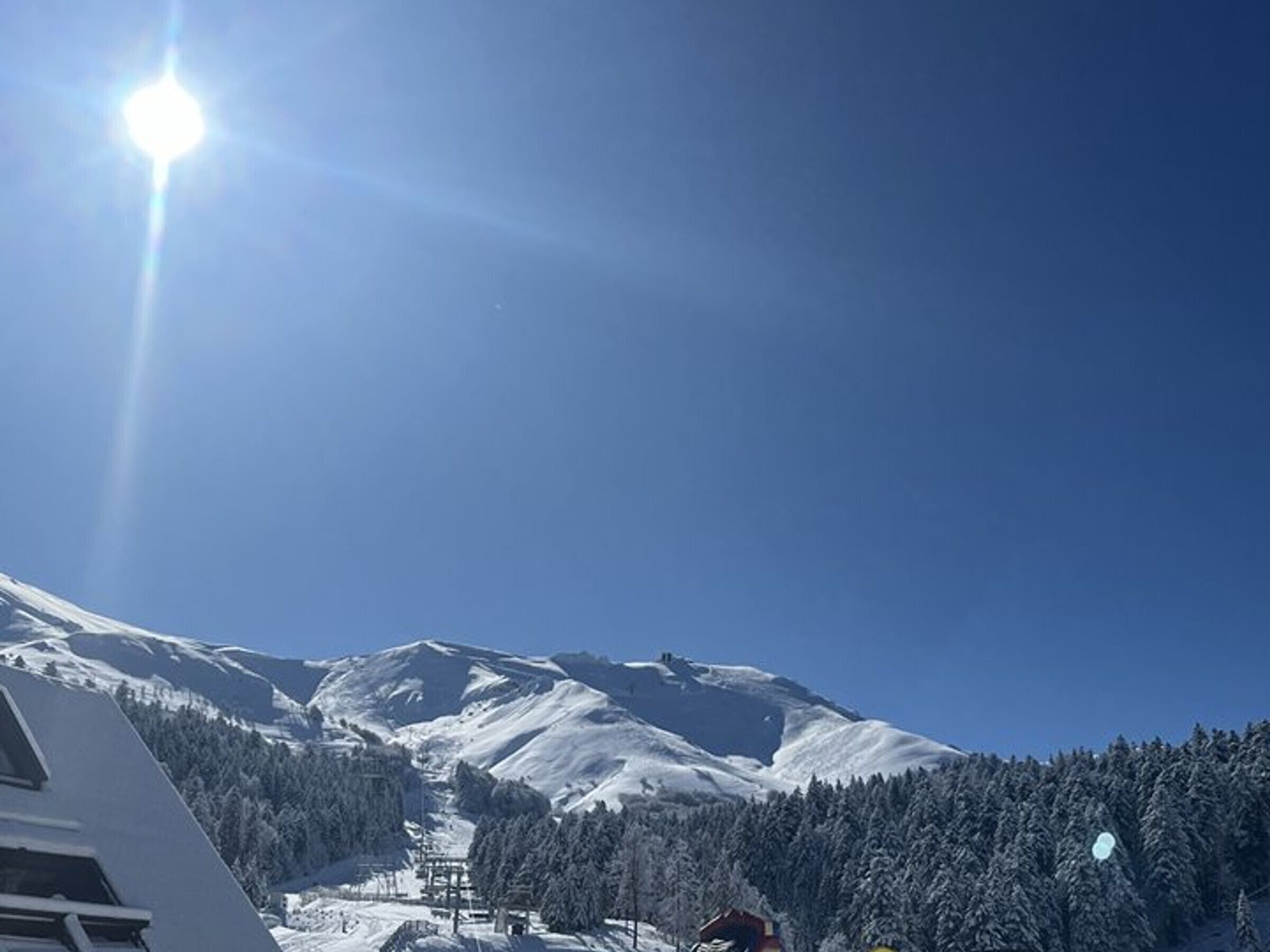 Ett snötäckt berg med en skidlift och en byggnad i förgrunden.