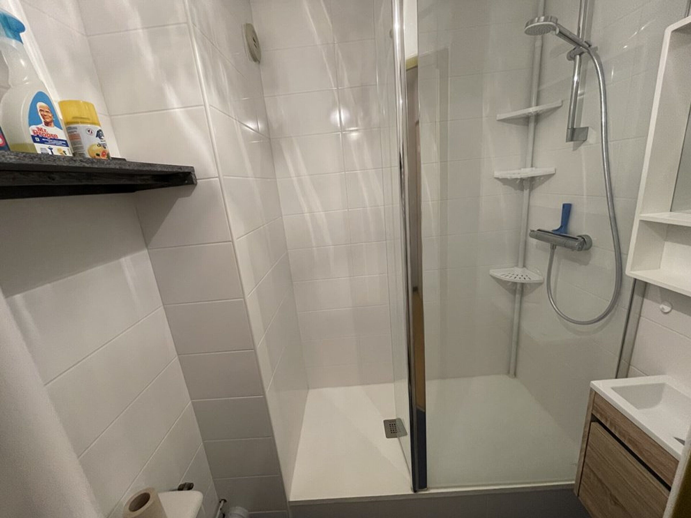 A modern bathroom with a glass-enclosed shower, white tiled walls, and a wooden vanity with a sink.