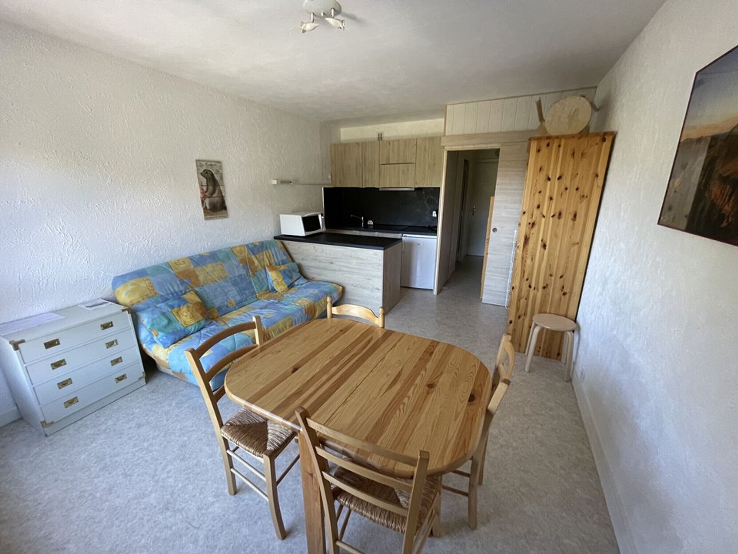 A compact living space with a kitchenette, a sofa, a dining table, and a small stool.