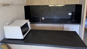 A compact kitchen with wooden cabinets, a black countertop, a white microwave, and a sink.