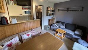 A compact living space with a kitchenette, a sofa, a dining table, and a bookshelf.