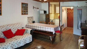 A cozy living room with a sofa, a dining table, and a kitchen in the background.