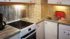 A compact kitchen with white cabinets, a wooden countertop, a black stove, and a red dish rack.
