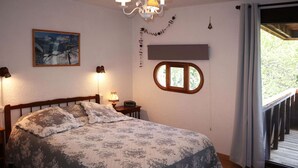 A bedroom with a bed, a nightstand, a wall-mounted lamp, a framed picture, a window, and a balcony.