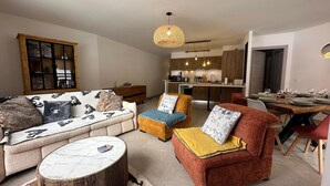 A modern living room with a sofa, ottoman, and coffee table, a dining area with a table set for four, and a kitchen in the background. - Apartment Vars, 3 bedrooms, 8 persons (Vars)