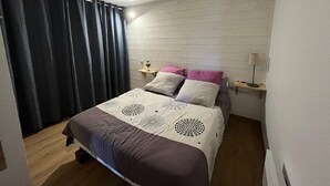 A bedroom with a bed, a bedside table, a lamp, and a window with curtains. - Renovated 2-bedroom apartment with terrace in Les Angles (Les Angles)