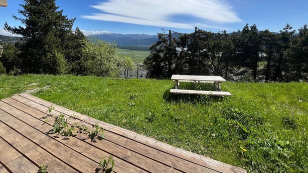 A wooden deck with a picnic table and benches overlooking a grassy area with trees and distant mountains. - Renovated 2-bedroom apartment with terrace in Les Angles (Les Angles)