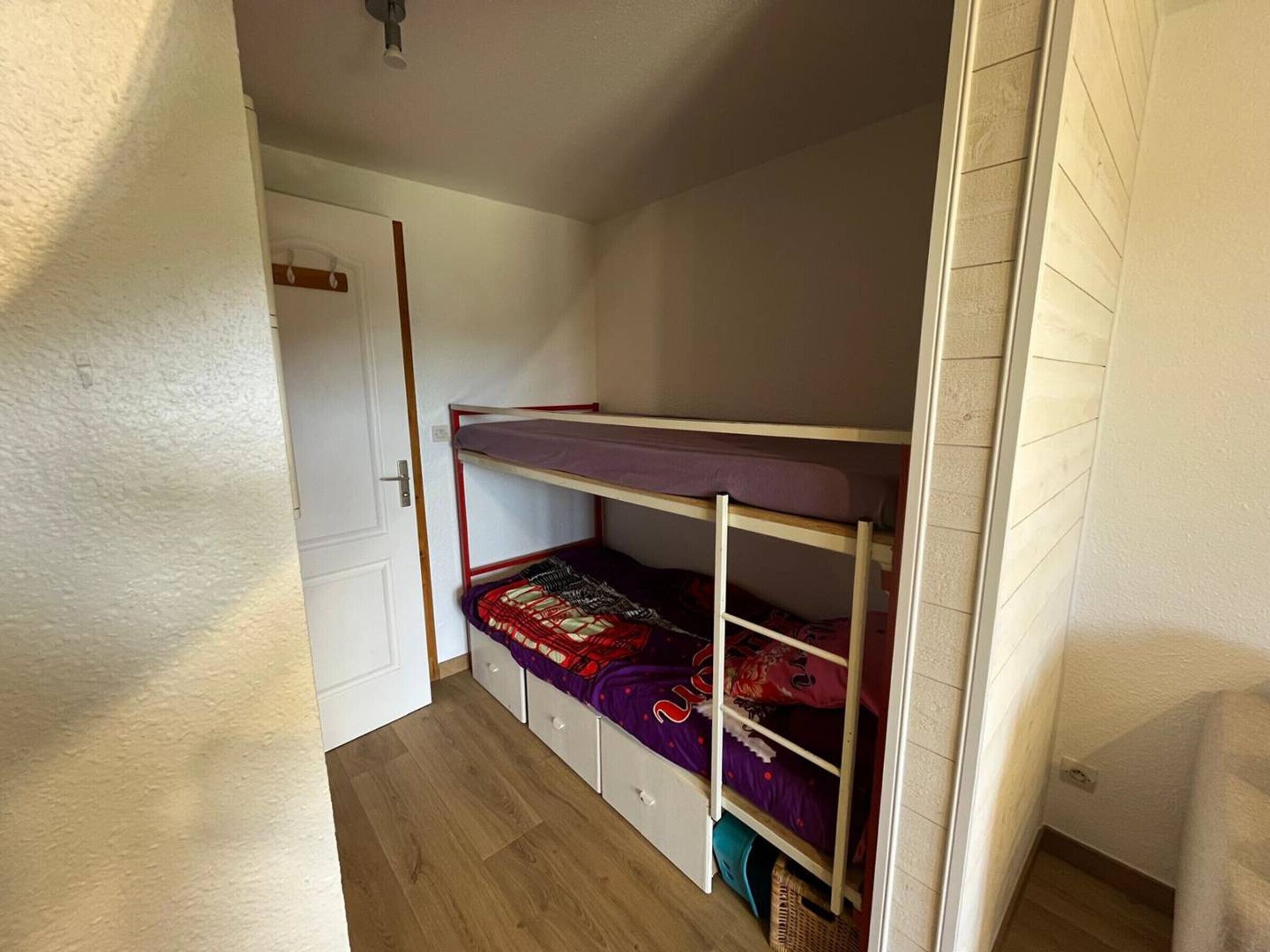 A small, compact room with a bunk bed, a white door, and a wooden floor.