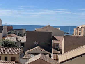 Ein Küstenwohngebiet mit terrakottafarbenen Dächern, blauem Himmel und Blick auf das Meer.