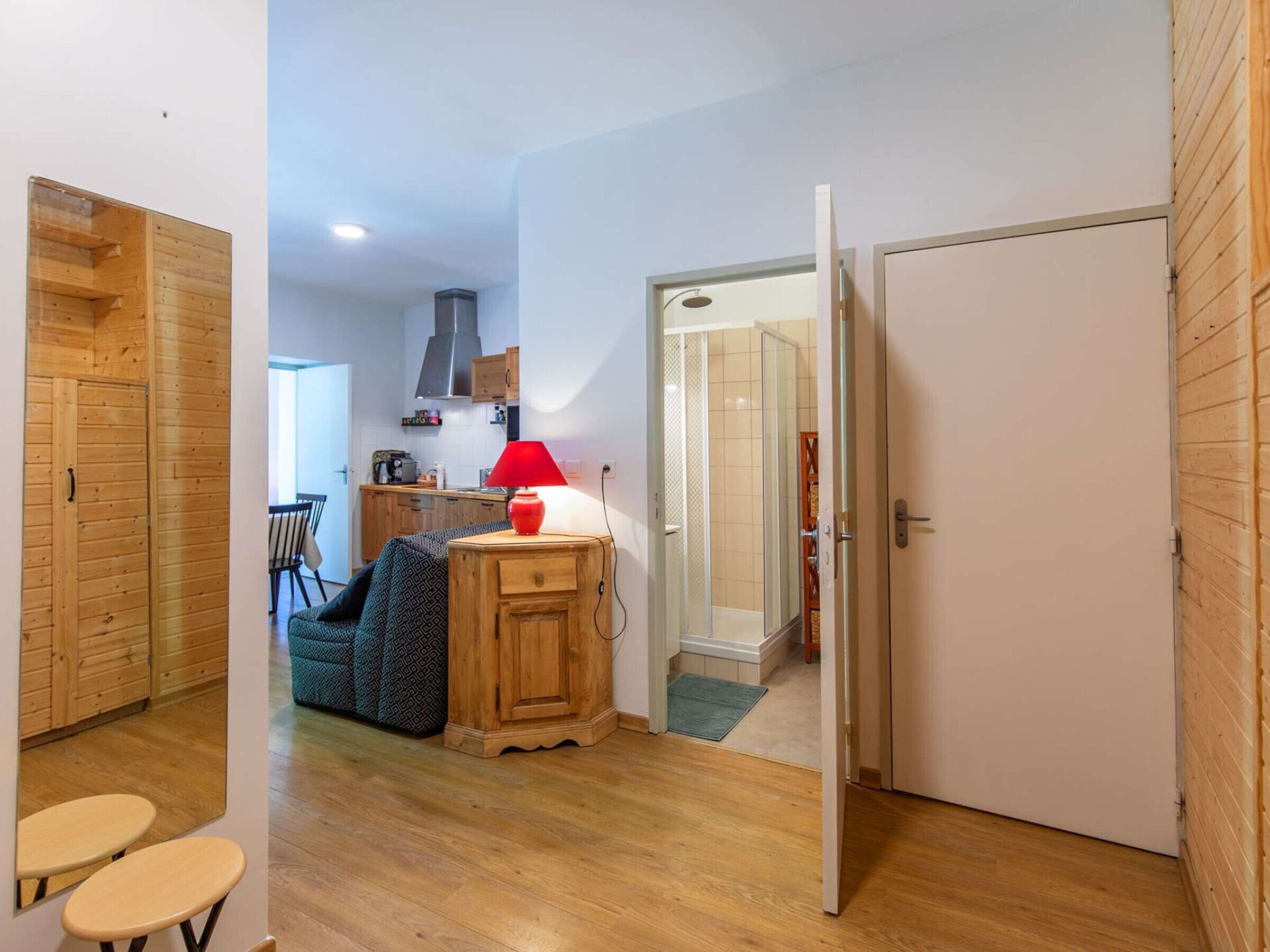 Un espace de vie compact comprenant un coin cuisine, une armoire en bois, un petit coin salon et une porte donnant accès à une salle de bain.