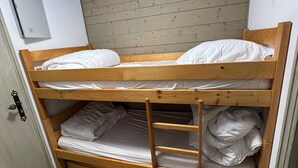 Un lit superposé à deux niveaux, avec une échelle en bois et un matelas blanc sur chaque lit.